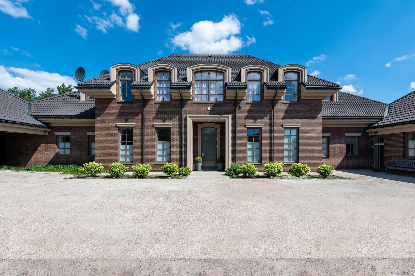 Brick manor with pale cast stone door surround, window heads and dormer trim under a blue sky