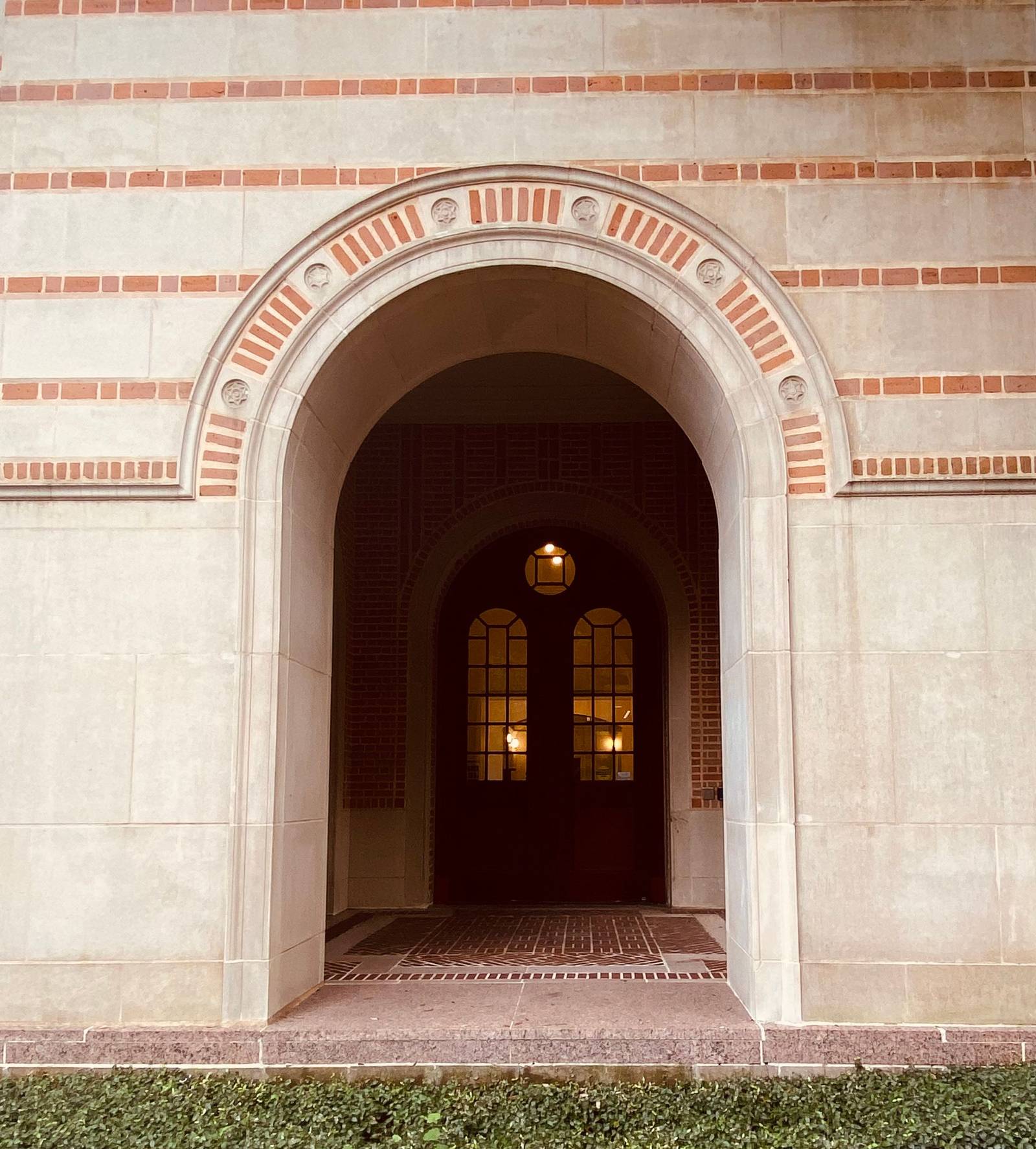 Arched entry framed by a smooth cast stone surround with inset brick voussoirs and brick banding