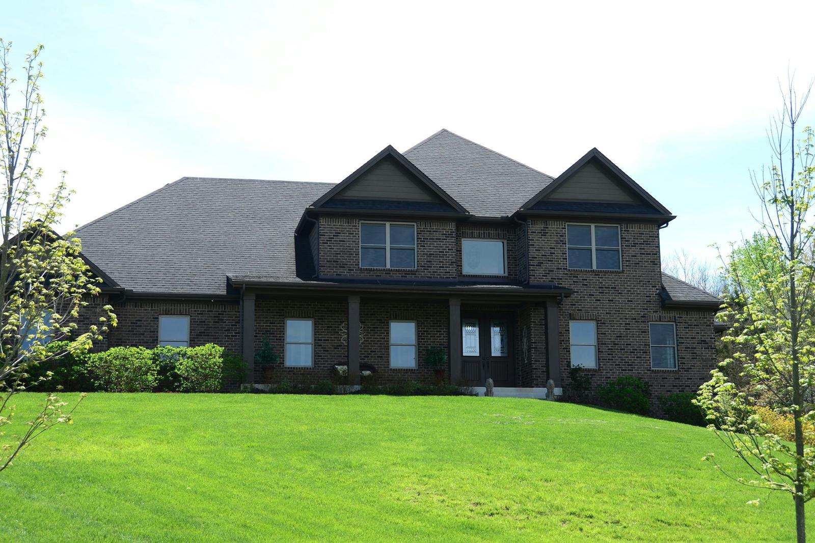 Large two-story brick custom home with dark gables and a covered front porch on a sloping lawn