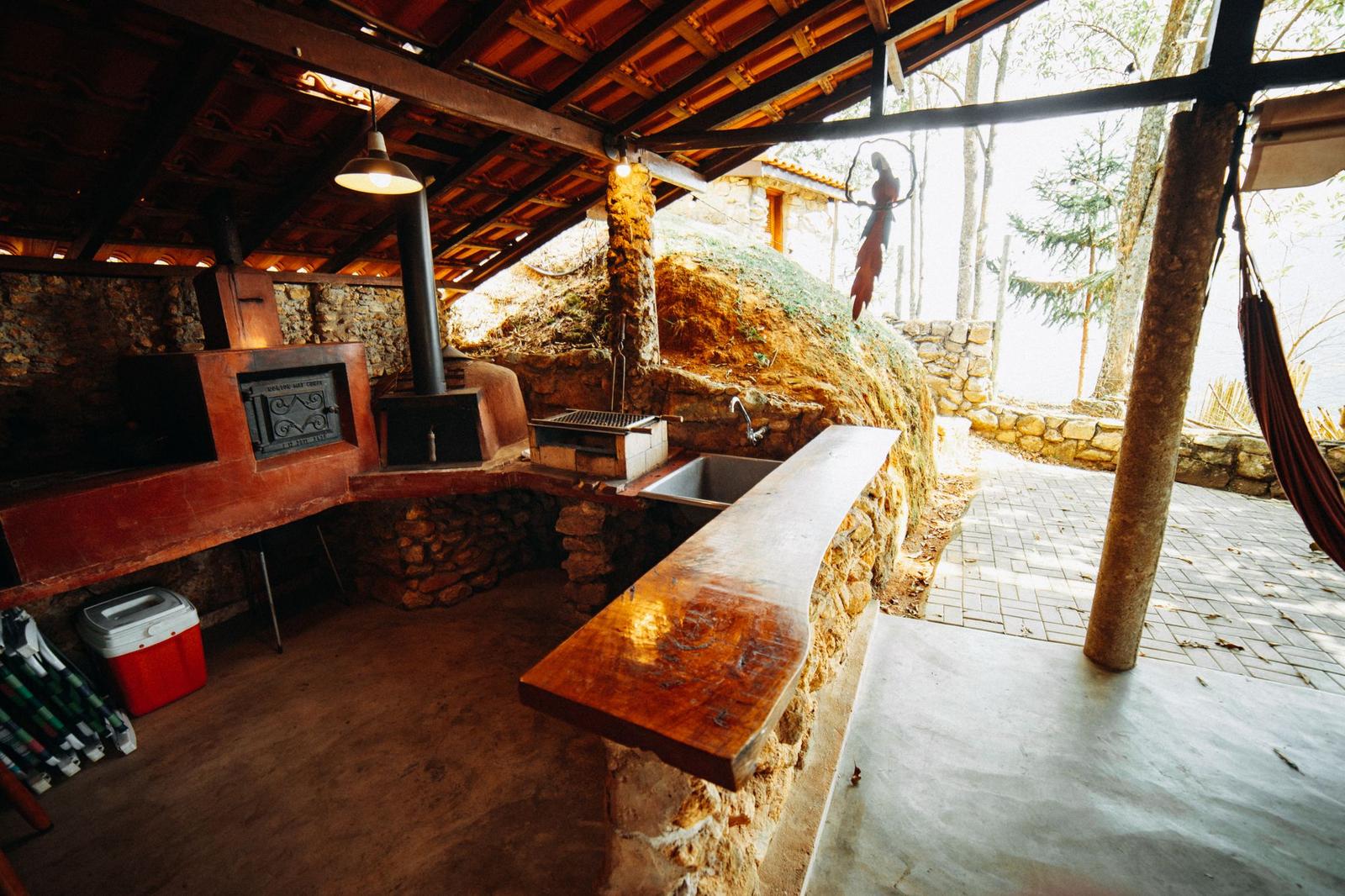 Covered outdoor kitchen with a stone-clad counter, built-in grill, sink and wood-fired oven
