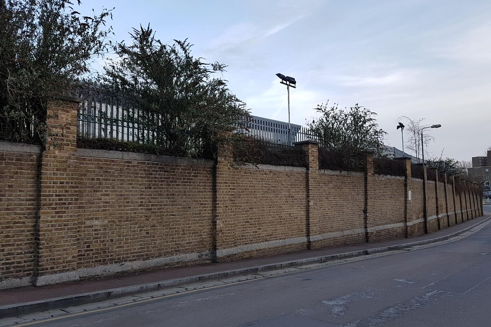 Long tan brick perimeter wall with evenly spaced piers running along a curving street