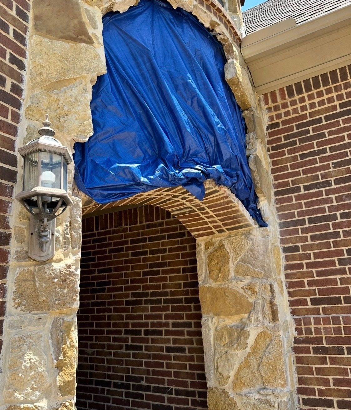 Close-up of the entry arch during the repair, under a blue tarp above the brick arch