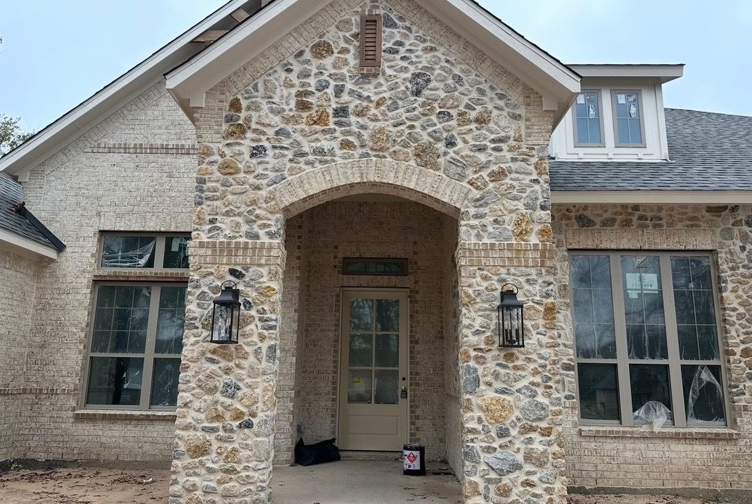 Front of a new home with a rough natural stone entry arch set into light brick walls