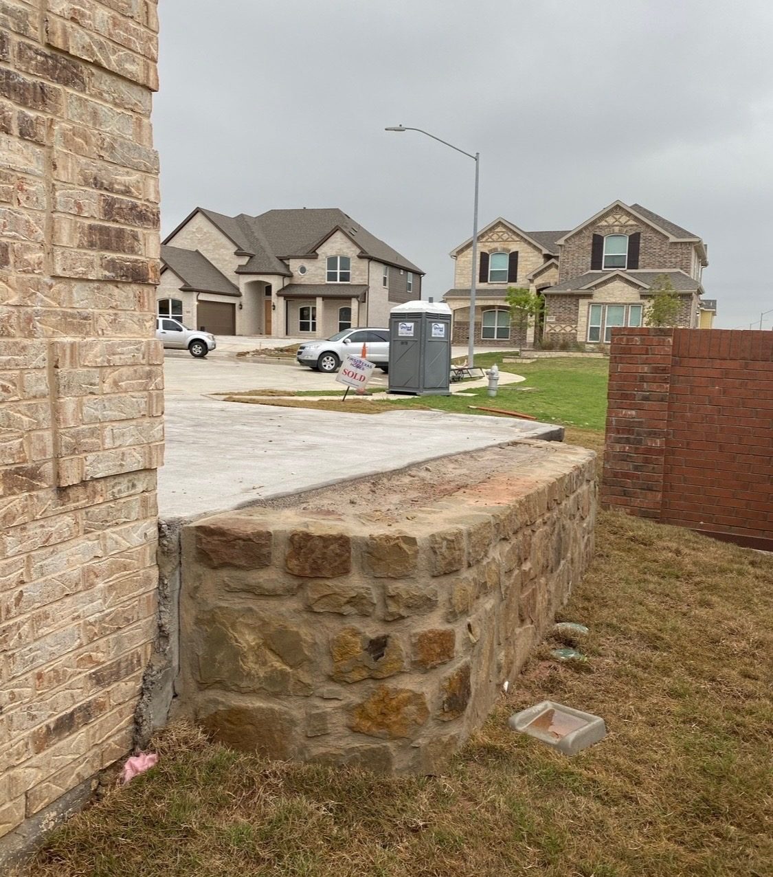 Curved natural stone retaining wall at the corner of a raised slab beside a brick house in a new subdivision