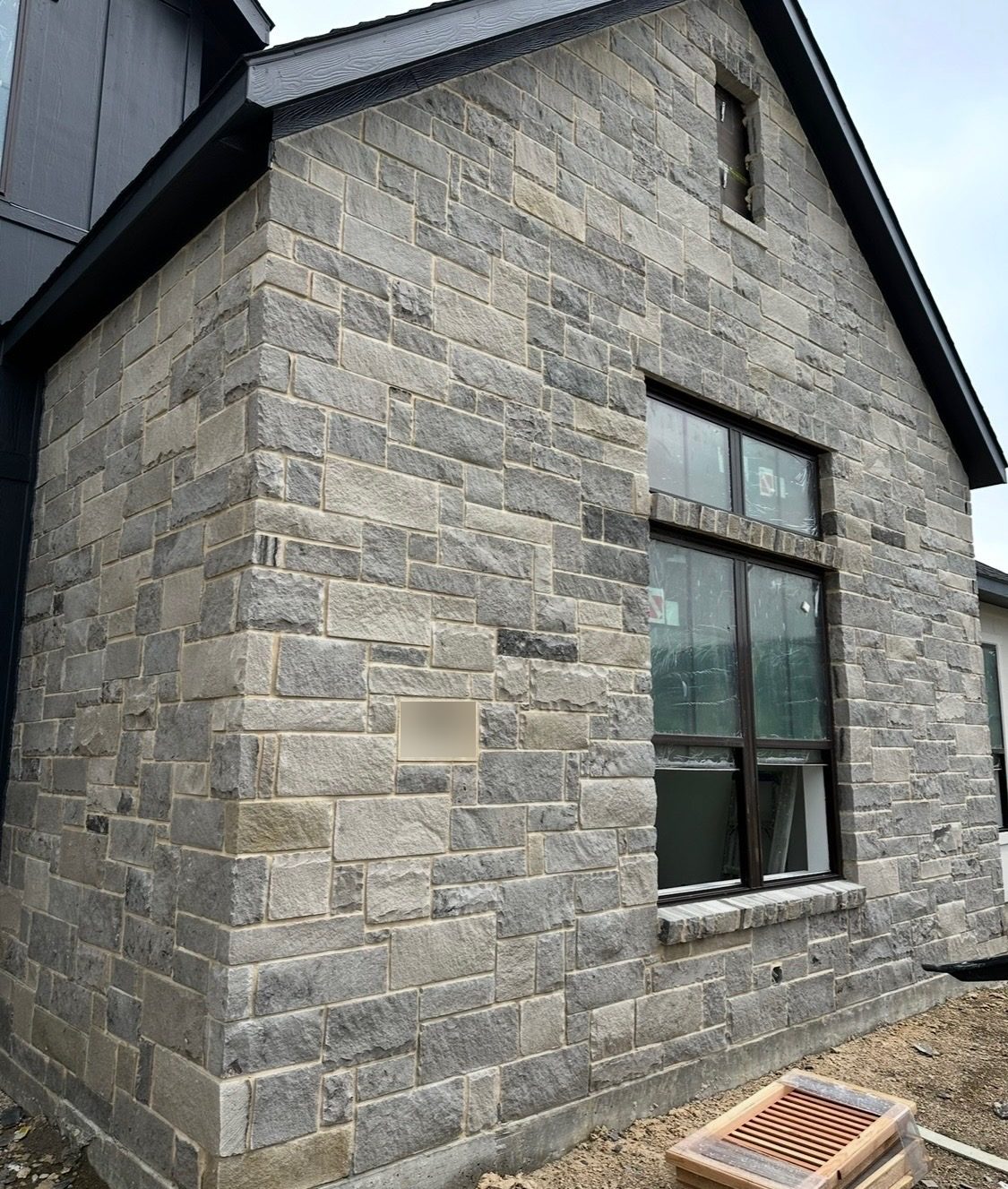 Corner of a new home clad in gray cut stone in mixed course heights, with a tall window and a stone address plaque
