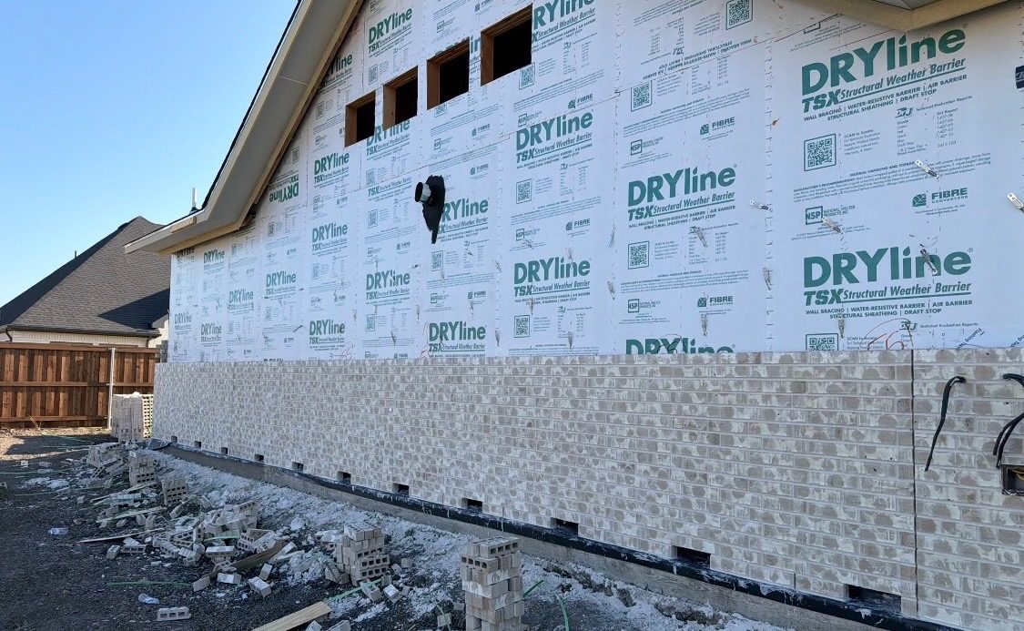 Stone base being laid along the bottom of a new house, below the weather barrier