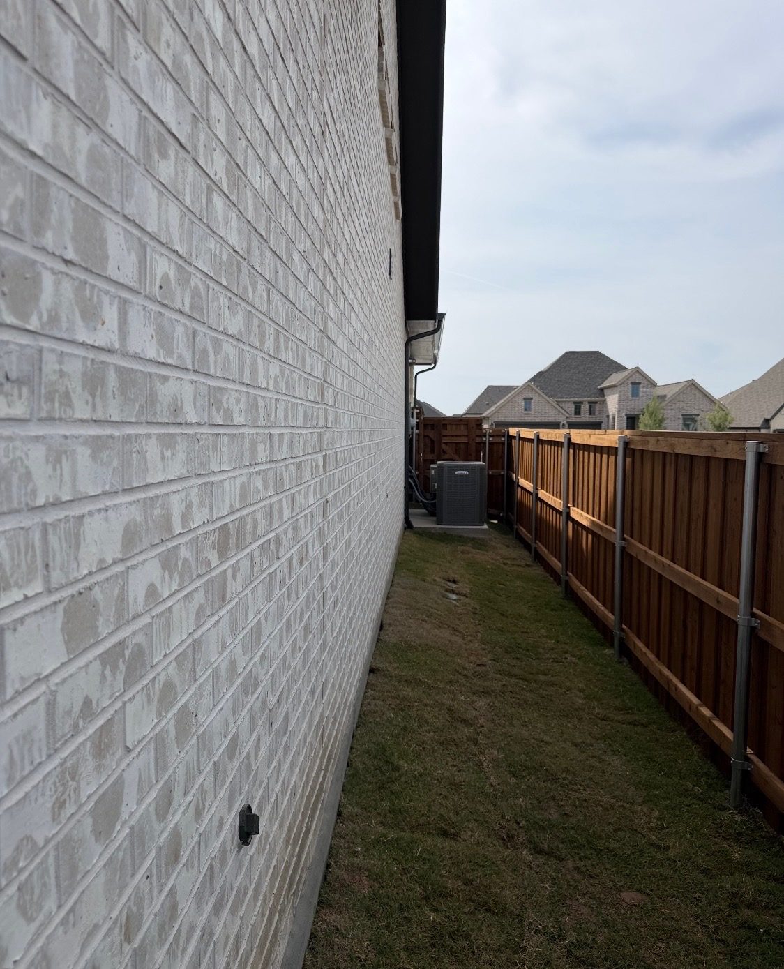 Long light brick side wall of the house, running straight past a wood fence