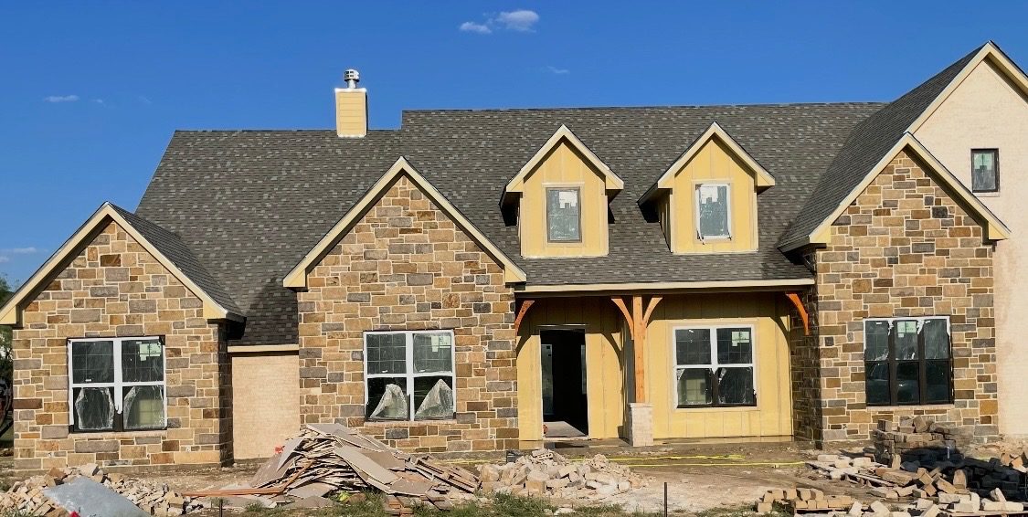 Front of a new home with brown stone on three gables and the garage, before final cleanup