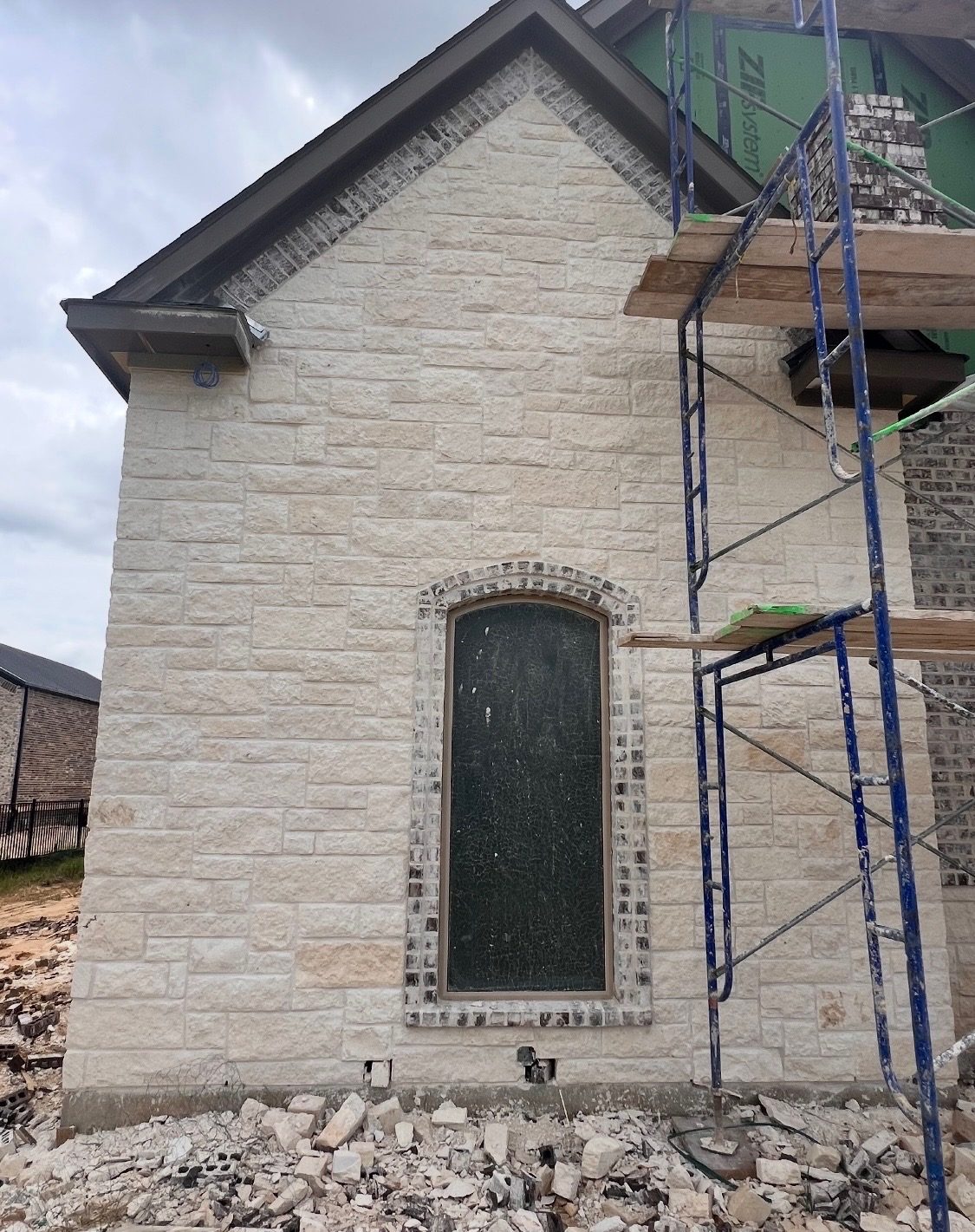 Light stone gable on a new home with a brick surround around a tall arched window, scaffolding still up