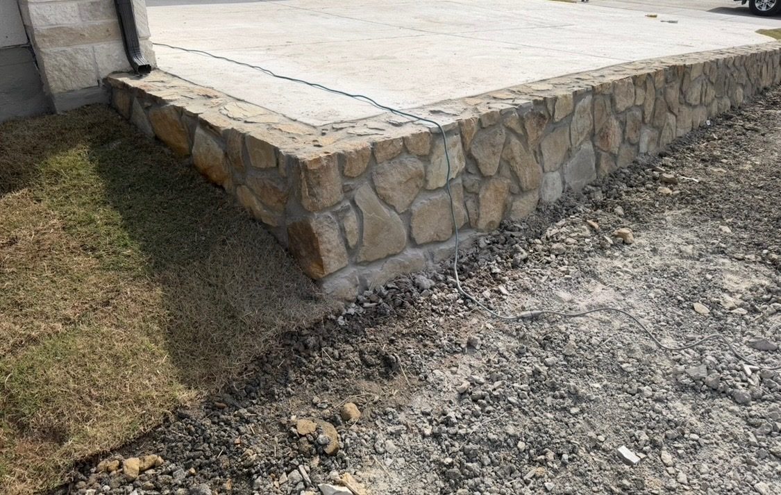 Natural stone retaining wall along the edge of a concrete slab on a freshly graded lot