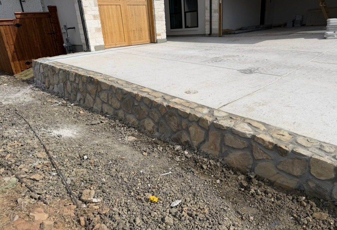 The stone retaining wall running along the slab in front of a garage with wood doors